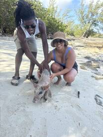 A couple interacts with a friendly pig on the beach, showcasing a unique wildlife experience in the Bahamas.