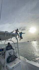 Two friends leap off the top of a boat into the water at sunset, capturing the thrill of a fun day on the water.