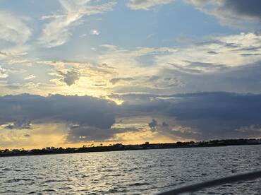 A stunning sunset casts golden hues over the water, creating a picturesque backdrop of the coastline — perfect for capturing the beauty of a tranquil evening on the water.