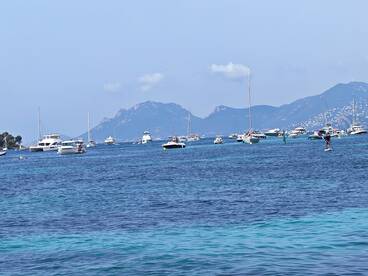 A vibrant scene of various boats and a paddleboarder enjoying the clear waters, showcasing the beauty of a coastal getaway.