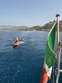 A thrilling moment as a person enjoys tubing behind a boat, with a stunning coastal backdrop — perfect for adventure seekers on the water.