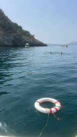 Swimmers enjoy the clear waters near a rocky coastline, with boats anchored in the background — a perfect scene for a summer day on the water.
