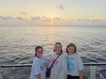 A joyful group of three poses for a photo against a stunning sunset backdrop while enjoying their time on the water — perfect for family outings or sunset cruises.
