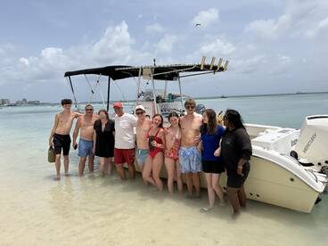 A cheerful group of friends enjoys a day at the beach, posing by their boat in shallow waters — a perfect moment of summer fun and adventure.