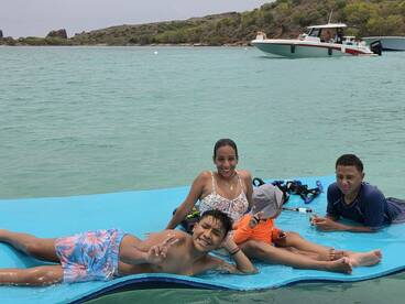 A joyful family enjoys a fun day in the water, relaxing on a floating mat while snorkeling gear is nearby — perfect for memorable aquatic adventures.