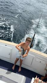 A young boy proudly holds up his catch while fishing on a boat, showcasing the joy of a successful day on the water.