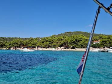 A picturesque view of a Croatian coastline with several boats anchored near a sandy beach, showcasing the beauty of summer outings on the water.