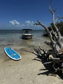 A serene view of a boat anchored near a sandy beach, with a paddleboard resting on the shore, perfect for a day of relaxation and water activities.