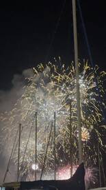 A stunning display of fireworks lights up the night sky, framed by the masts of nearby boats — a perfect backdrop for festive celebrations on the water.