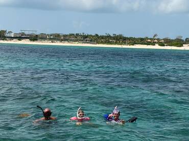 A family enjoys snorkeling in crystal-clear waters, surrounded by a beautiful beach backdrop — perfect for aquatic adventures and family bonding.