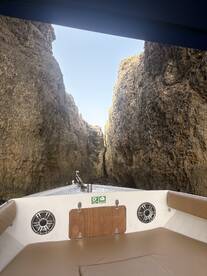 A stunning view from the bow of a boat navigating through a narrow passage between towering rock formations, showcasing the beauty of the surrounding landscape.