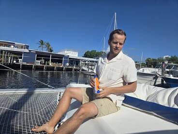 A man relaxes on the deck of a boat, applying sunblock while enjoying a sunny day by the water — perfect for leisure and relaxation on the water.