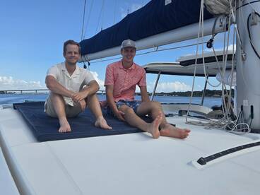 Two friends relax on the deck of a catamaran, enjoying a sunny day on the water — perfect for social outings and leisure adventures.