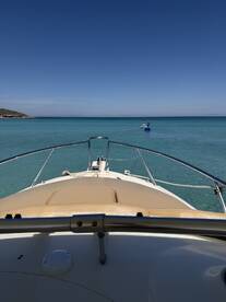 A scenic view from the bow of a boat, showcasing a paddleboarder enjoying the clear turquoise waters — perfect for water sports enthusiasts.