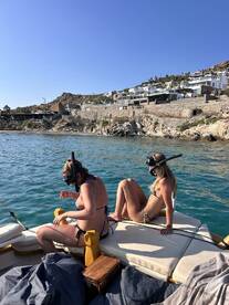 Two friends prepare for snorkeling while relaxing on the deck of a boat, surrounded by beautiful coastal scenery — a perfect day for aquatic adventures.