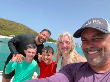 A joyful family poses for a selfie on a boat, enjoying their time in the water — a perfect moment capturing fun and togetherness on a sunny day.