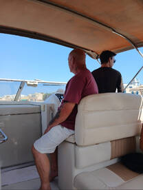 Two individuals are seated inside the helm area of a boat, enjoying the view and the experience of being on the water.