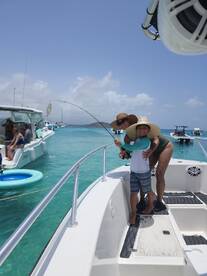 A joyful family moment on a fishing trip, capturing a child and adult celebrating a catch aboard a boat in beautiful turquoise waters.