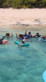 A lively group enjoys a fun day floating in the clear waters, perfect for relaxation and beach activities.