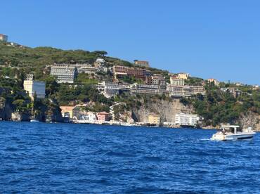 A scenic view of a boat cruising along a picturesque coastline, showcasing beautiful cliffs and vibrant buildings — perfect for exploring the stunning Amalfi Coast.
