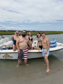A lively group of friends enjoys a fun day at the beach, posing on their boat while wading in the water — perfect for summer adventures and memorable outings.