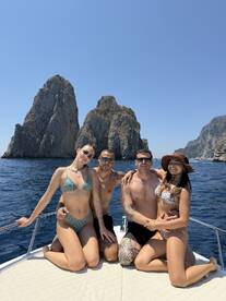 A cheerful group of friends poses on the deck of a boat, surrounded by stunning rock formations and clear blue waters — perfect for summer adventures and memorable outings.