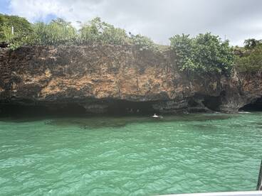 A scenic view of swimmers exploring a cave in clear turquoise waters, showcasing the beauty of the natural landscape and adventure on the water.