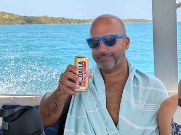 A man enjoys a refreshing drink while relaxing on a boat, surrounded by beautiful turquoise waters — perfect for a day of leisure and celebration.
