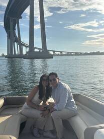 A couple enjoys a sunny day on a boat, smiling together with a scenic bridge in the background — perfect for romantic outings or special celebrations on the water.