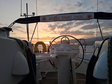 A serene view of the helm area aboard a sailing vessel, showcasing the beautiful sunset over the water — perfect for a relaxing sailing experience.