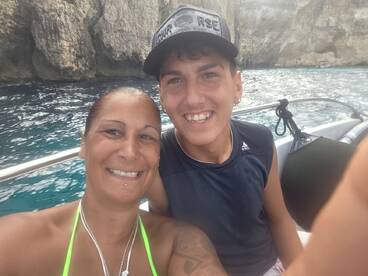 A joyful moment captured on a boat, showcasing a smiling woman and a young boy against a scenic backdrop of rocky cliffs and clear waters.