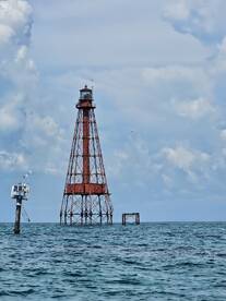 A striking lighthouse stands tall in the ocean, surrounded by tranquil waters and a picturesque sky, making it a perfect landmark for boating adventures.