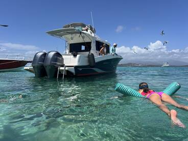 A child enjoys swimming with pool floats near a boat in clear turquoise waters, capturing the essence of a fun day on the water.