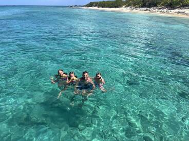 A joyful group of friends enjoys a refreshing swim in the crystal-clear waters, perfect for family outings and beach adventures.