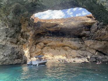 A scenic view of a boat near a stunning cave, with guests enjoying the water — a perfect spot for swimming and exploration.