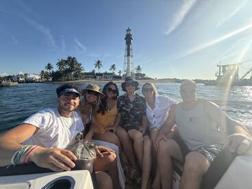 A cheerful group of friends enjoys a day on the water, posing in front of a picturesque lighthouse — perfect for memorable boating adventures.