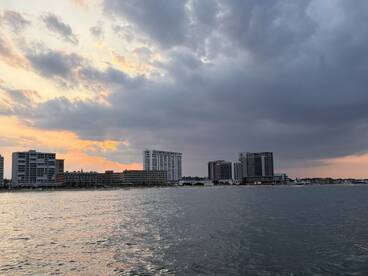 A scenic view of a waterfront with buildings and a cloudy sky at sunset, creating a tranquil atmosphere.