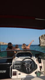A group of friends enjoys a scenic boat ride, pointing towards a stunning rock formation along the coastline — perfect for adventure seekers and nature lovers.