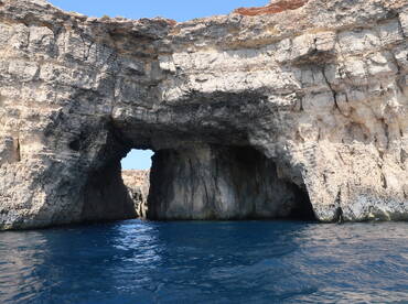A stunning view of a natural rock formation with an arch, showcasing the beautiful coastline and clear blue waters — a perfect highlight for boating adventures.