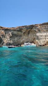 A picturesque scene featuring several boats anchored near a stunning rocky coastline, with people enjoying the clear turquoise waters — perfect for a summer getaway.