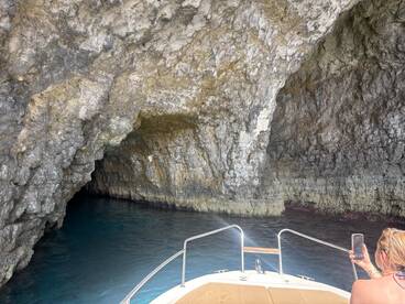 A scenic view of a boat approaching a stunning cave, with a guest capturing the moment on their phone — perfect for adventure seekers exploring hidden gems on the water.