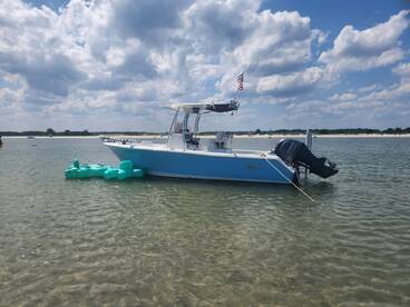 A sleek speedboat anchored in shallow waters, showcasing its vibrant blue hull against a backdrop of fluffy clouds and a sandy shoreline.