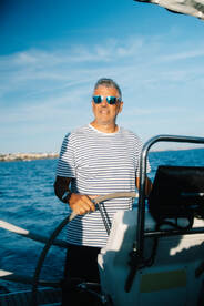 A confident captain navigates the waters while steering the helm of a sailboat, showcasing the joy of sailing adventures on the open sea.