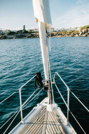 A stunning view from the bow of a sailboat, showcasing the vessel's sleek design against a backdrop of calm waters and coastal scenery.