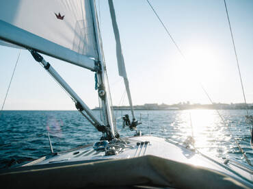 A stunning view from the deck of a sailboat, capturing the serene waters and the sun reflecting off the surface — perfect for sailing enthusiasts and sunset lovers.