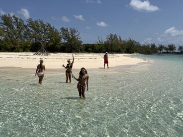 A lively group enjoys a sunny day at the beach, wading in crystal-clear waters while celebrating with drinks — a perfect tropical getaway.