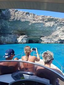 A group of friends enjoys a scenic view while capturing the moment on camera, with a stunning cave backdrop and crystal-clear waters — perfect for adventure seekers.