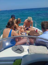 A lively group enjoys a meal on the deck of a boat, surrounded by stunning blue waters — perfect for social gatherings and memorable outings.