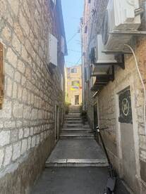 A narrow alleyway with stone walls and steps leading up, showcasing a quaint urban scene. Ideal for exploring local architecture and hidden gems.