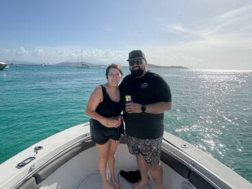 A couple enjoys drinks on the bow of their boat, surrounded by sparkling ocean waters — a perfect moment for celebration and relaxation on the water.